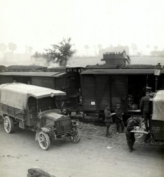 greyscale photo of vehicles beside train